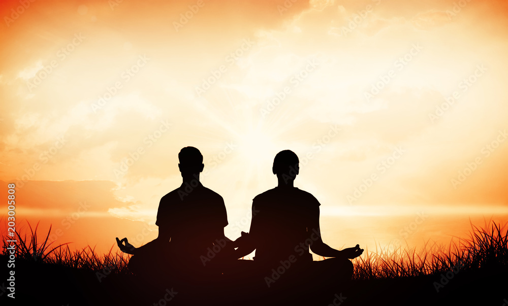 Attractive couple in white meditating in lotus pose against orange sunrise