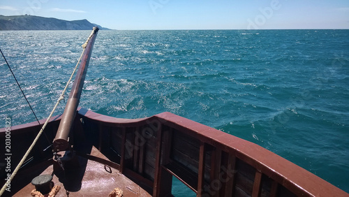 The ship sails along the sea along the high bank. The bright sun illuminates the bowsprit on the bow of the boat and waves on the sea photo