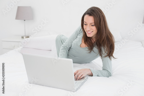 Relaxed casual young woman using laptop in bed
