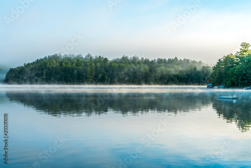 Early morning mist lifts off a small, reflective lake
