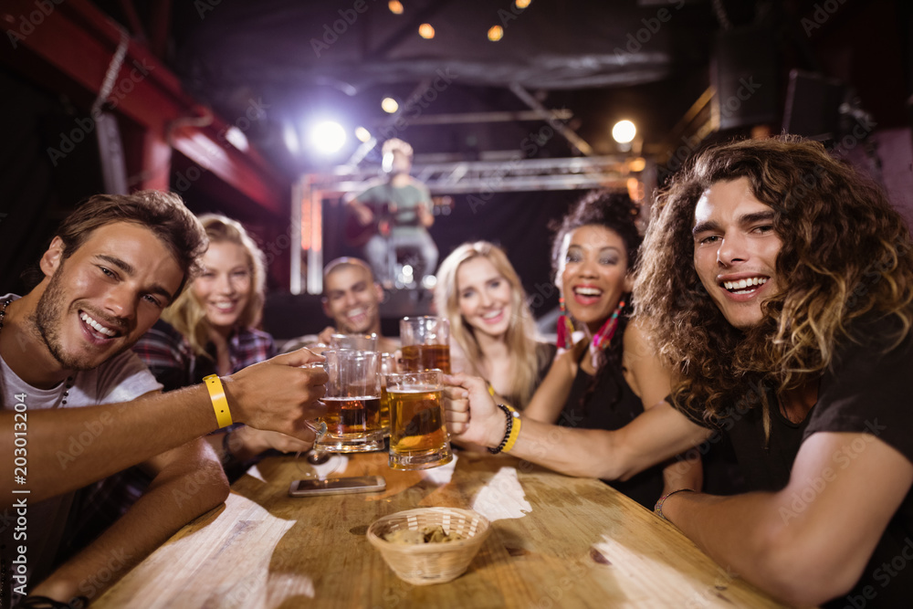 Portrait of happy friends toasting beer glasses while sitting at table