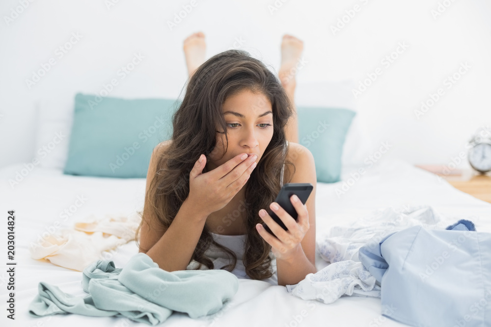 Shocked woman looking at mobile phone in bed Shocked woman looking at mobile phone in bed