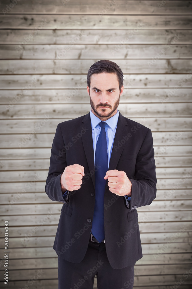Angry businessman with closed fists looking at camera against wooden planks background Angry businessman with closed fists looking at camera against wooden planks background