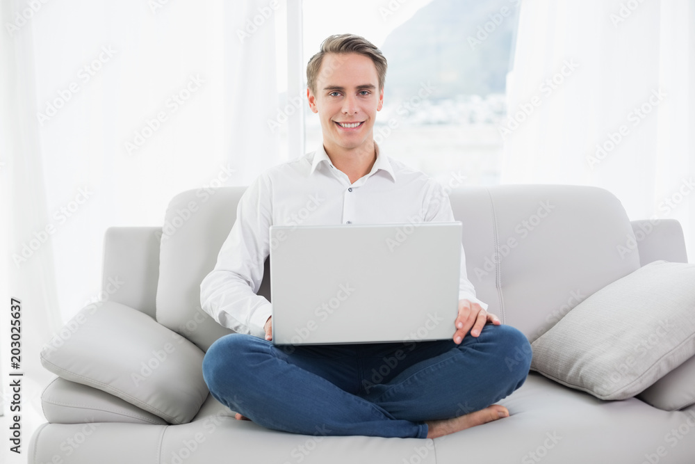 Smiling casual young man using laptop on sofa Smiling casual young man using laptop on sofa