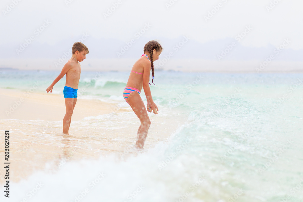 Brother and sister playing together on sea shore with waves. Family travel vacation concept background Brother and sister playing together on sea shore with waves. Family travel vacation concept background