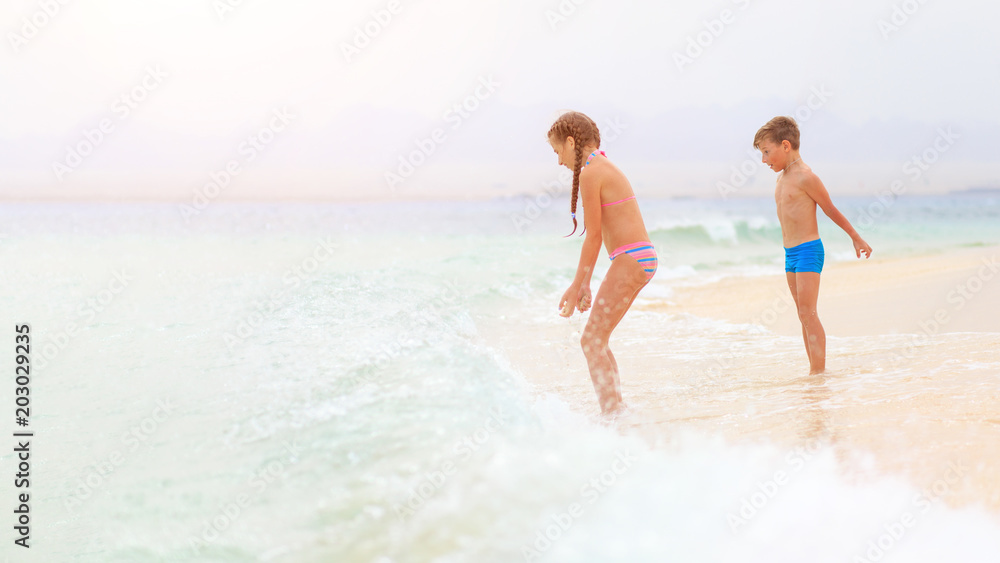 Brother and sister playing together on sea shore with waves. Family travel vacation concept background