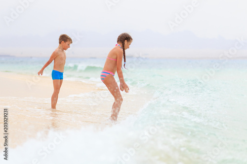 Brother and sister playing together on sea shore with waves. Family travel vacation concept background