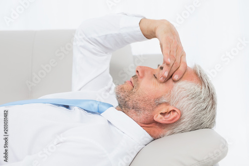 Tired mature businessman resting on sofa in living room