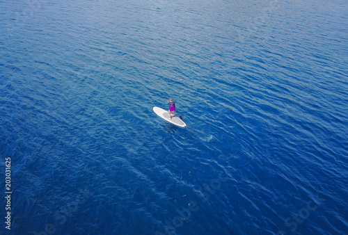 Aerial view of Unidentified women tourist paddling a surfboard to middle of the sea.
