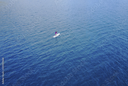 Aerial view of Unidentified women tourist paddling a surfboard to middle of the sea.