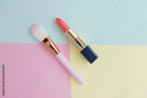 Flat lay of creative female decorative cosmetic for pink lipstick and pink cheek brush on the colorful background with copy space