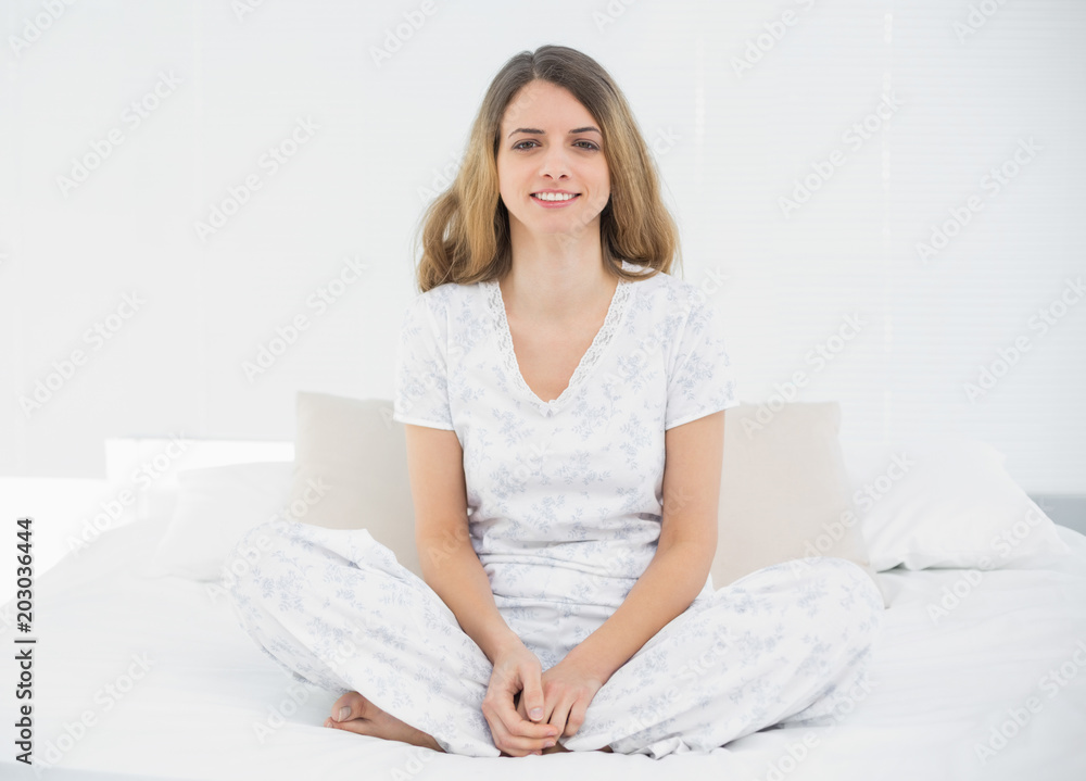 Content young woman wearing pyjamas sitting on her bed Content young woman wearing pyjamas sitting on her bed