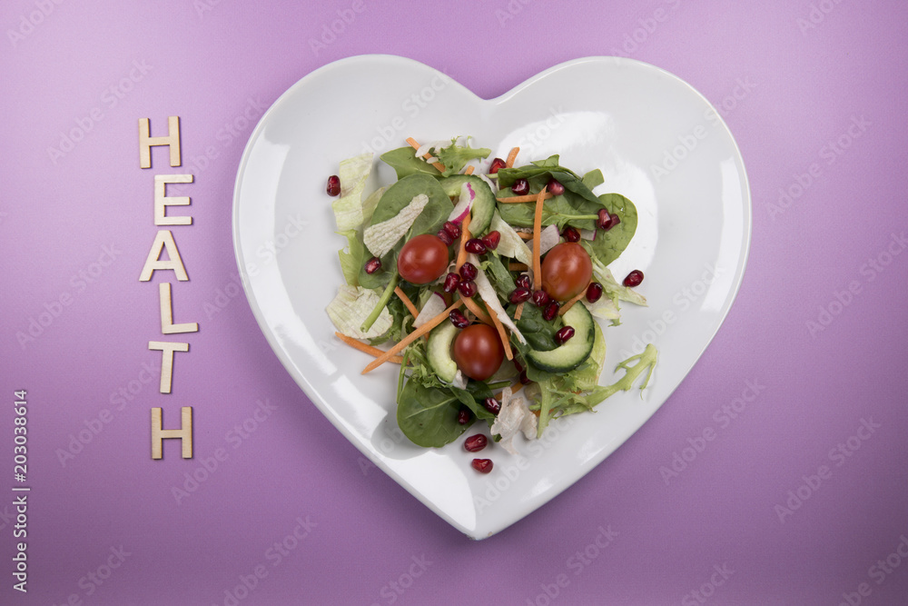 Traditional salad on a heart shaped plate with the word health in wooden letters Traditional salad on a heart shaped plate with the word health in wooden letters