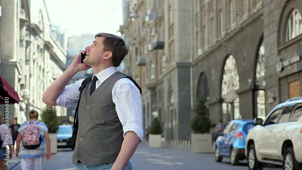 A tourist with a backpack is on a European street. A man is talking by the phone and telling what he sees around him. Tourist considers sights A tourist with a backpack is on a European street. A man is talking by the phone and telling what he sees around him. Tourist considers sights
