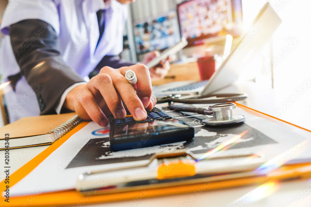 Fototapeta premium Healthcare costs and fees concept.Hand of smart doctor used a calculator and tablet for medical costs at modern hospital in sun light