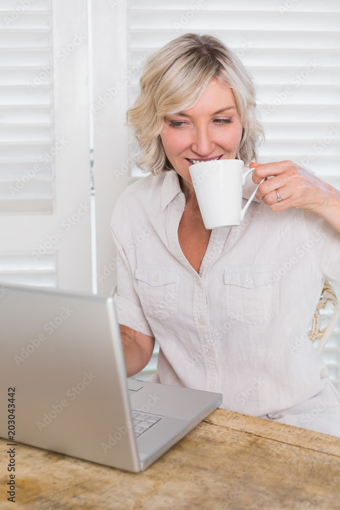 Mature woman drinking coffee while using laptop Mature woman drinking coffee while using laptop