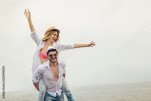 Happy couple in love on beach summer vacations. Joyful girl piggybacking on young boyfriend having fun.