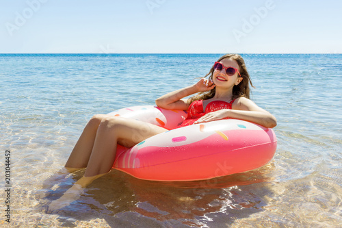 happy Young girl in a sprinkled donut float in the sea, smiling with sunglasses for summer
