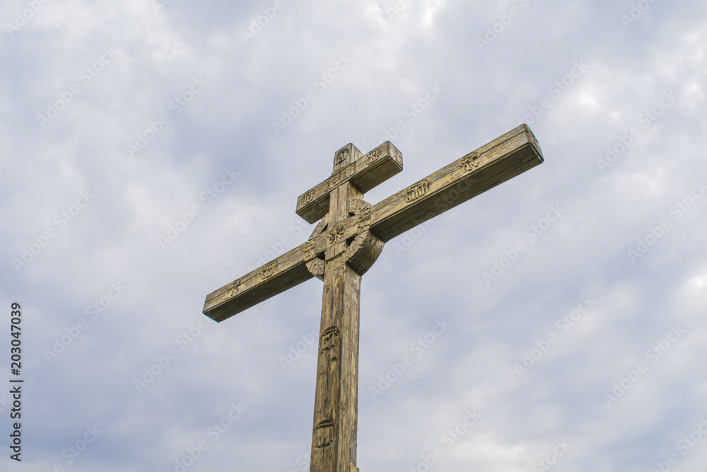 A wooden cross on top of a hill. Orthodox white cross glows on the top of the hill on the background of blue sky