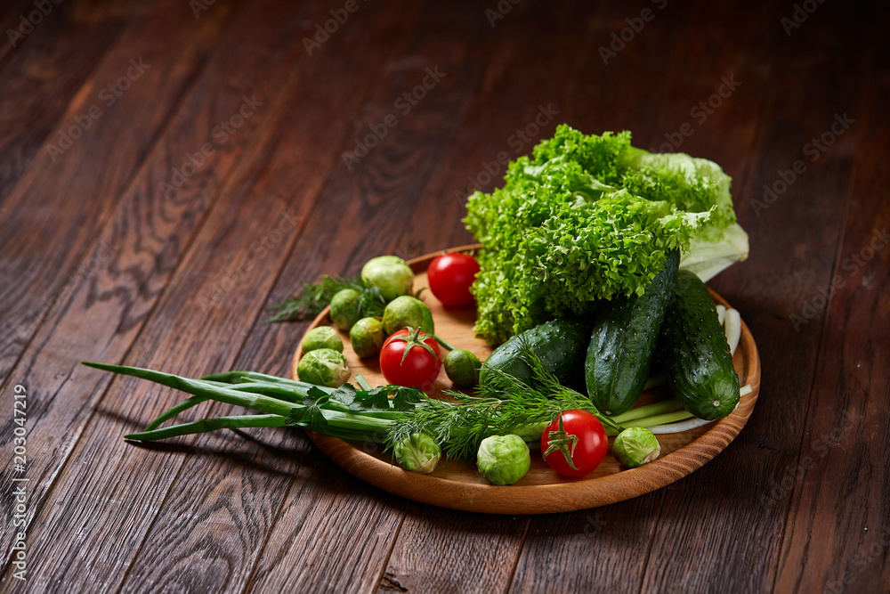 Vegetarian still life of fresh vegetables on wooden plate over rustic background, close-up, flat lay.