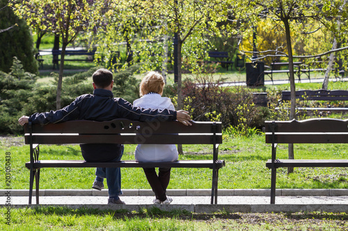 Couple in love is sitting on a bench in the park. Back view