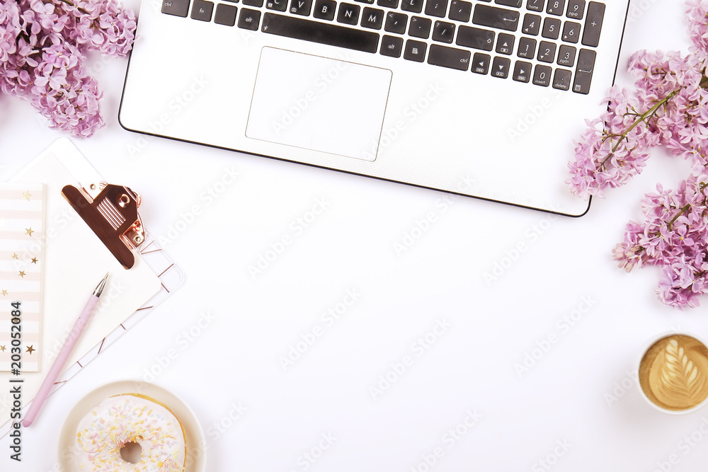 Feminine desktop, close up, laptop keyboard, blank clipboard, coffee and donut, lilac flowers. Flat lay composition, notebook computer, pen, cappuccino cup, purple bouquet white background. Copy space