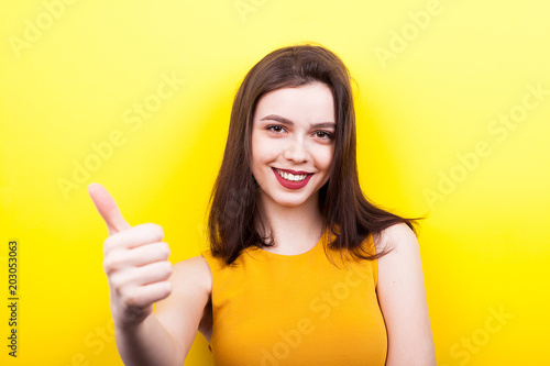 Beautiful woman showing thumbs up on yellow background