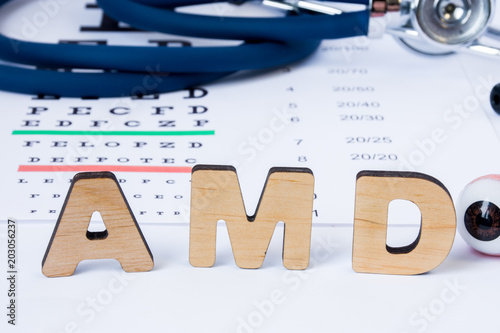 AMD Abbreviation or acronym of age-related macular degeneration - eye problem in older persons. Word AMD is on foreground near eye model with stethoscope and visual acuity test on blurry background photo