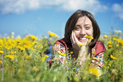 A smiling brown hair woman in a flowered field in a sunny day.