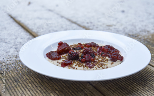 Vegan semolina porridge presented on wooden table with snow in the background. The porridge has berries and seeds on top.