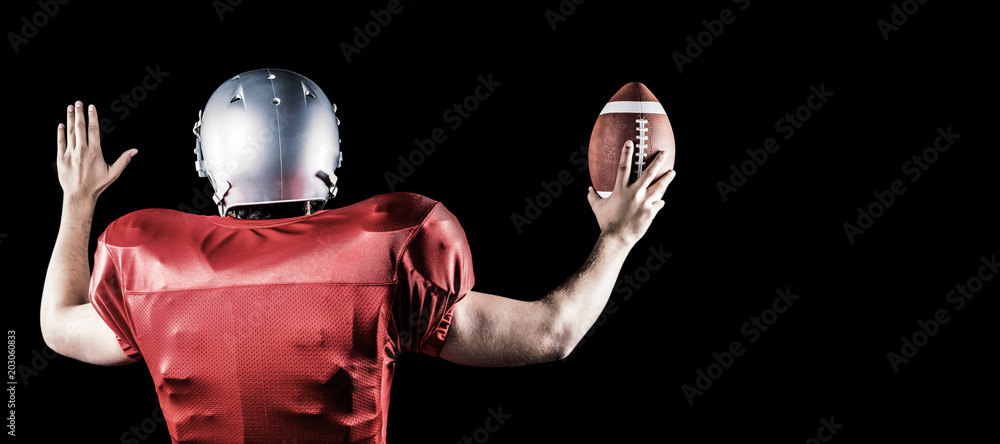 Rear view of American football player gesturing while holding ball against black