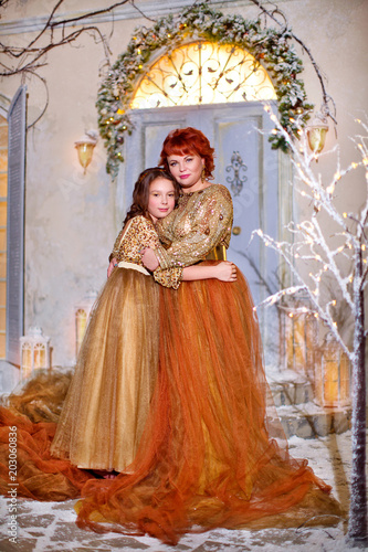 Charming red-haired mother hugging beautiful daughter, on background of door near house