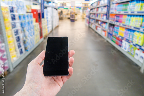Hand with mobile phone on a background of a blurry shopping center