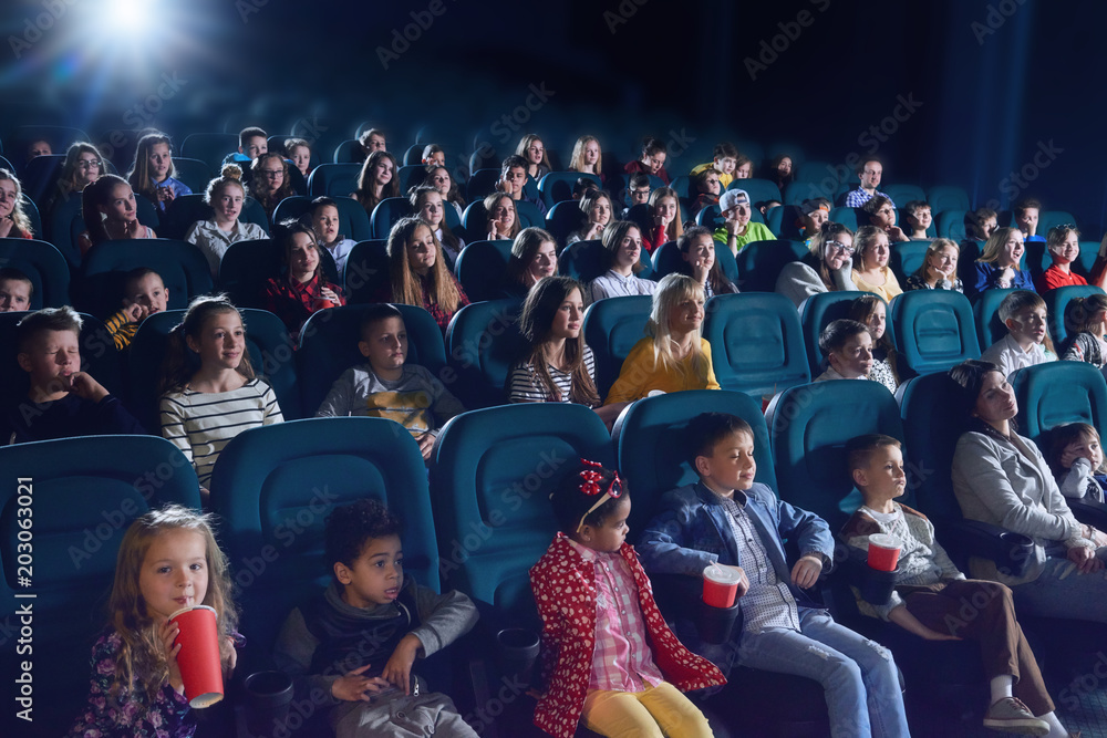 Crowd of people sitting in comfortable seats in modern movie theatre