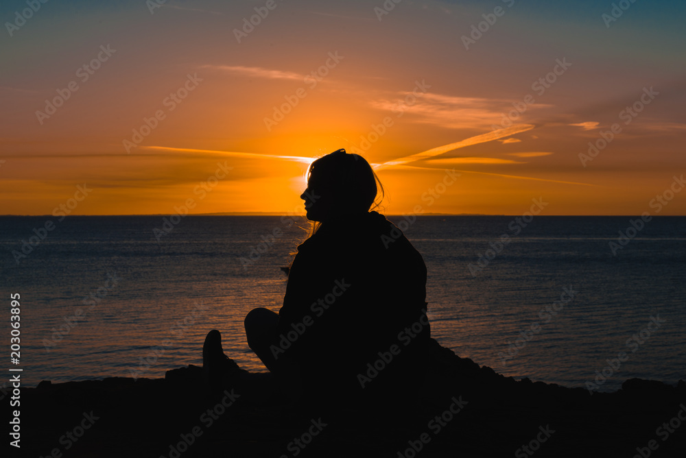 Female silhouette in front of a seaside sunset