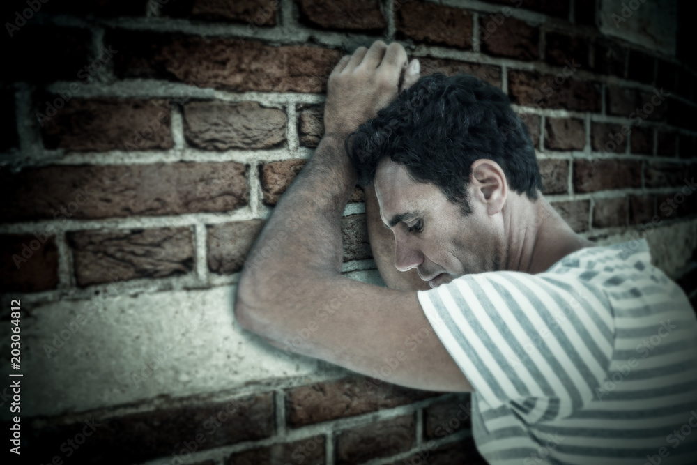 Upset man leaning on white background against red brick wall