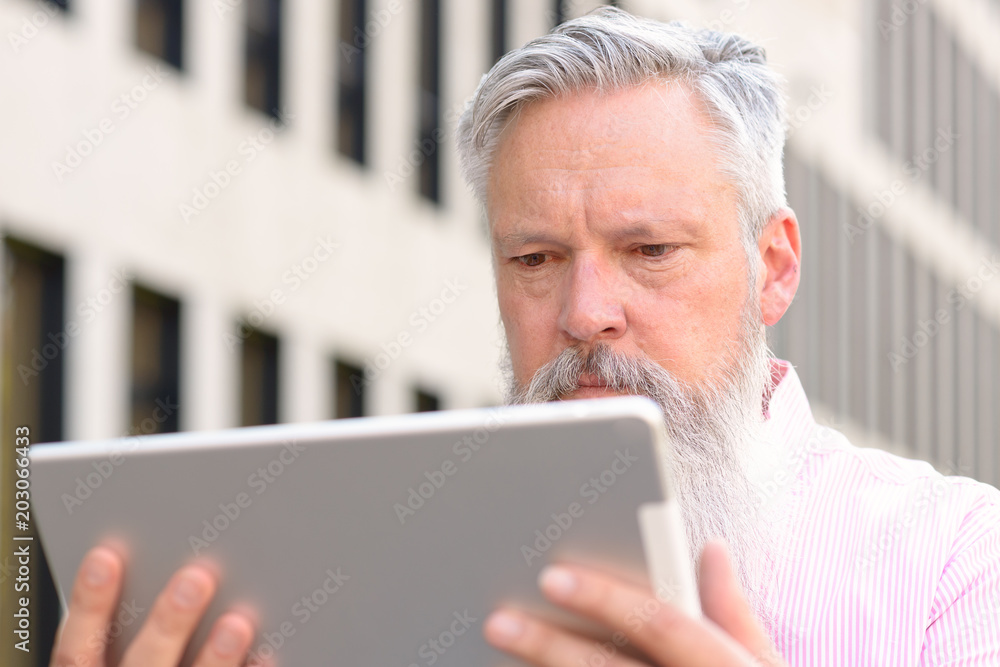 Grey-haired bearded man reading on a tablet Grey-haired bearded man reading on a tablet