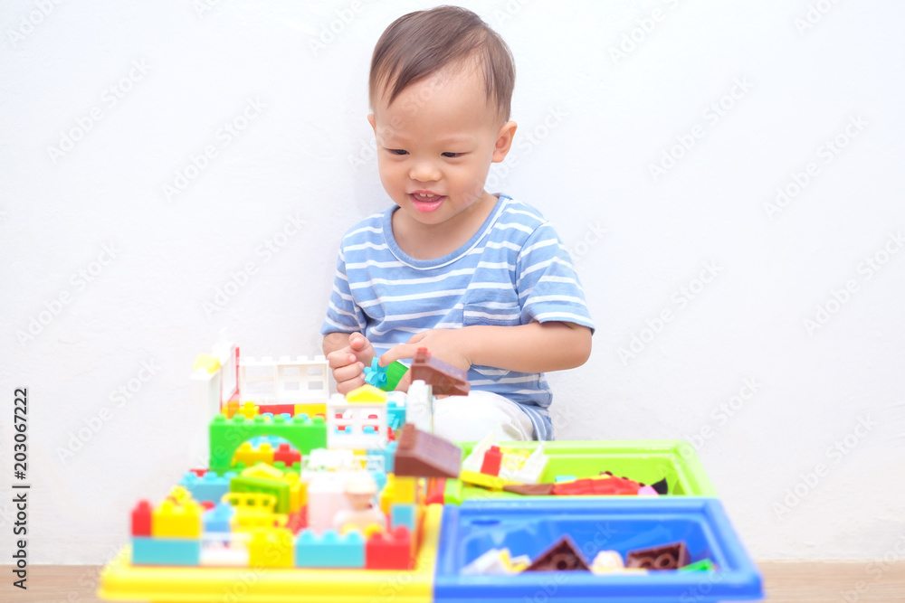 Cute little Asian 18 months / 1 year old toddler boy child sitting on wooden floor having fun playing with colorful building blocks indoor at home, Educational toys for young children concept Cute little Asian 18 months / 1 year old toddler boy child sitting on wooden floor having fun playing with colorful building blocks indoor at home, Educational toys for young children concept