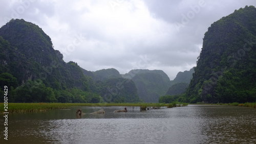 Mountains covered by trees frame a river under cloudy sky