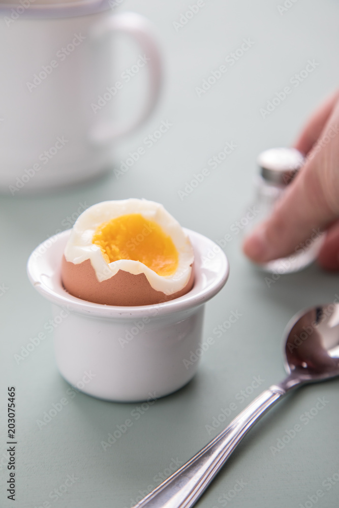 Offenes Ei mit Eigelb im Eierbecher mit Salzstreuer, Eierlöffel und Kaffee Offenes Ei mit Eigelb im Eierbecher mit Salzstreuer, Eierlöffel und Kaffee