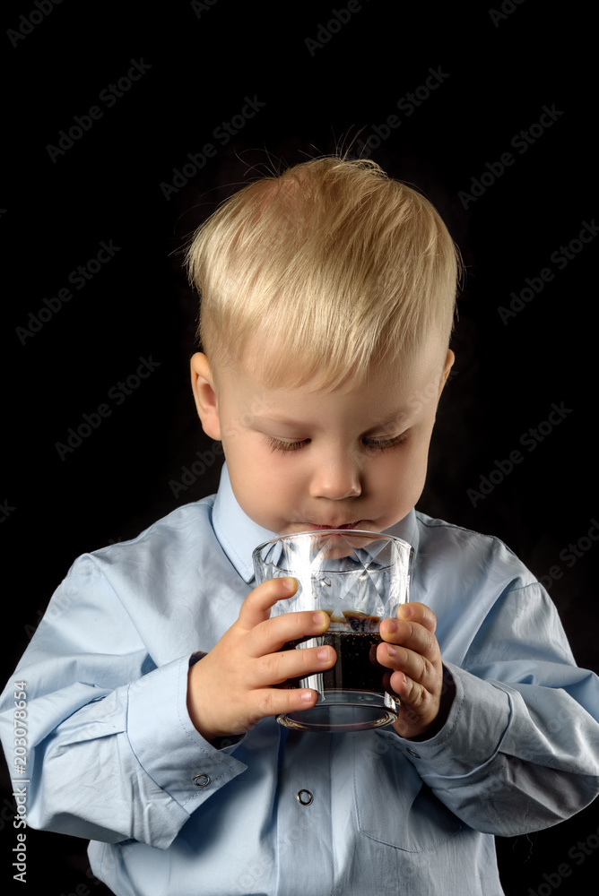 little boy drinks juice from a glass beaker on a dark background little boy drinks juice from a glass beaker on a dark background