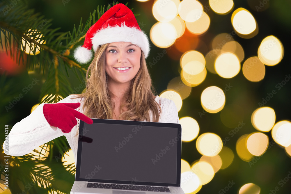 Festive blonde pointing to laptop against fir tree branch with green needles Festive blonde pointing to laptop against fir tree branch with green needles
