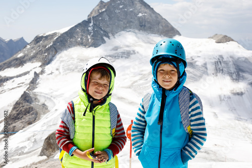Two little boys with safety helmets and clothing with mountains landscape backgrounds. Kids hiking and discovering glacier in Tirol, Austria, Hintertux