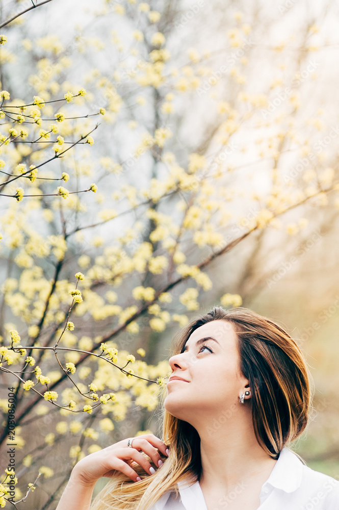 A portrait of a pretty young girl in a garden enjoying blooming trees with yellow flowers, romantically looking up, film grain effect A portrait of a pretty young girl in a garden enjoying blooming trees with yellow flowers, romantically looking up, film grain effect