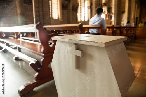 White donation box with a cross on it at a Christian church.  Collection box for generous offertory standing among pews at a Catholic temple photo