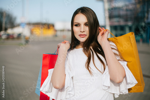 Pretty brunette with long hair stands with shopping bags before a modern glass building