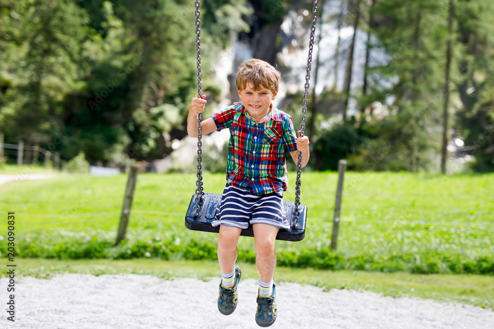 Funny kid boy having fun with chain swing on outdoor playground while being wet splashed with water Funny kid boy having fun with chain swing on outdoor playground while being wet splashed with water