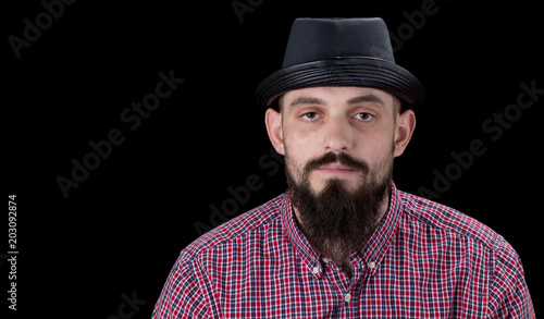 Pensive  bearded male dressed in a fleece shirt  and hat posing over black background © Oleksandr
