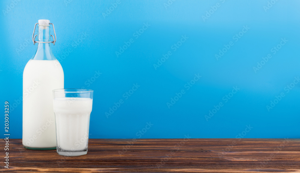 a glass of milk, a bottle of milk on a wooden table on a colored background a glass of milk, a bottle of milk on a wooden table on a colored background