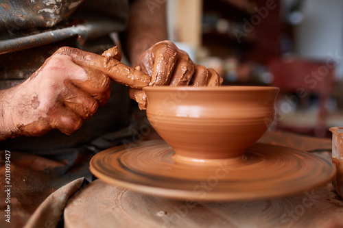 Close-up hands of a male potter in apron molds bowl from clay, selective focus